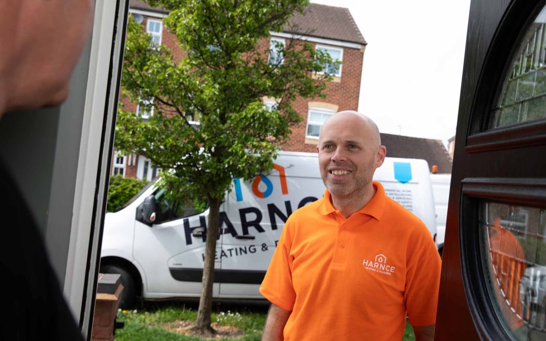 Photograph of male engineer at front door with logo on orange t-shirt and the branded Harnce van in the background